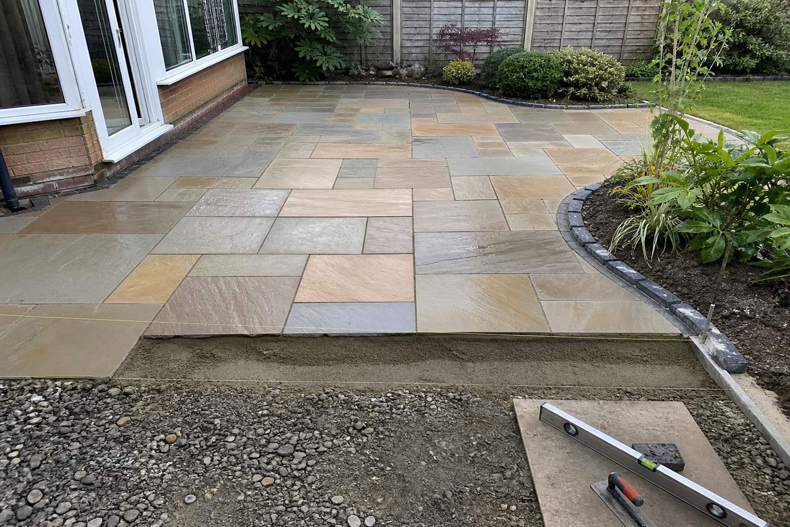 Patio installers setting natural stone slabs on a full mortar bed in a British garden